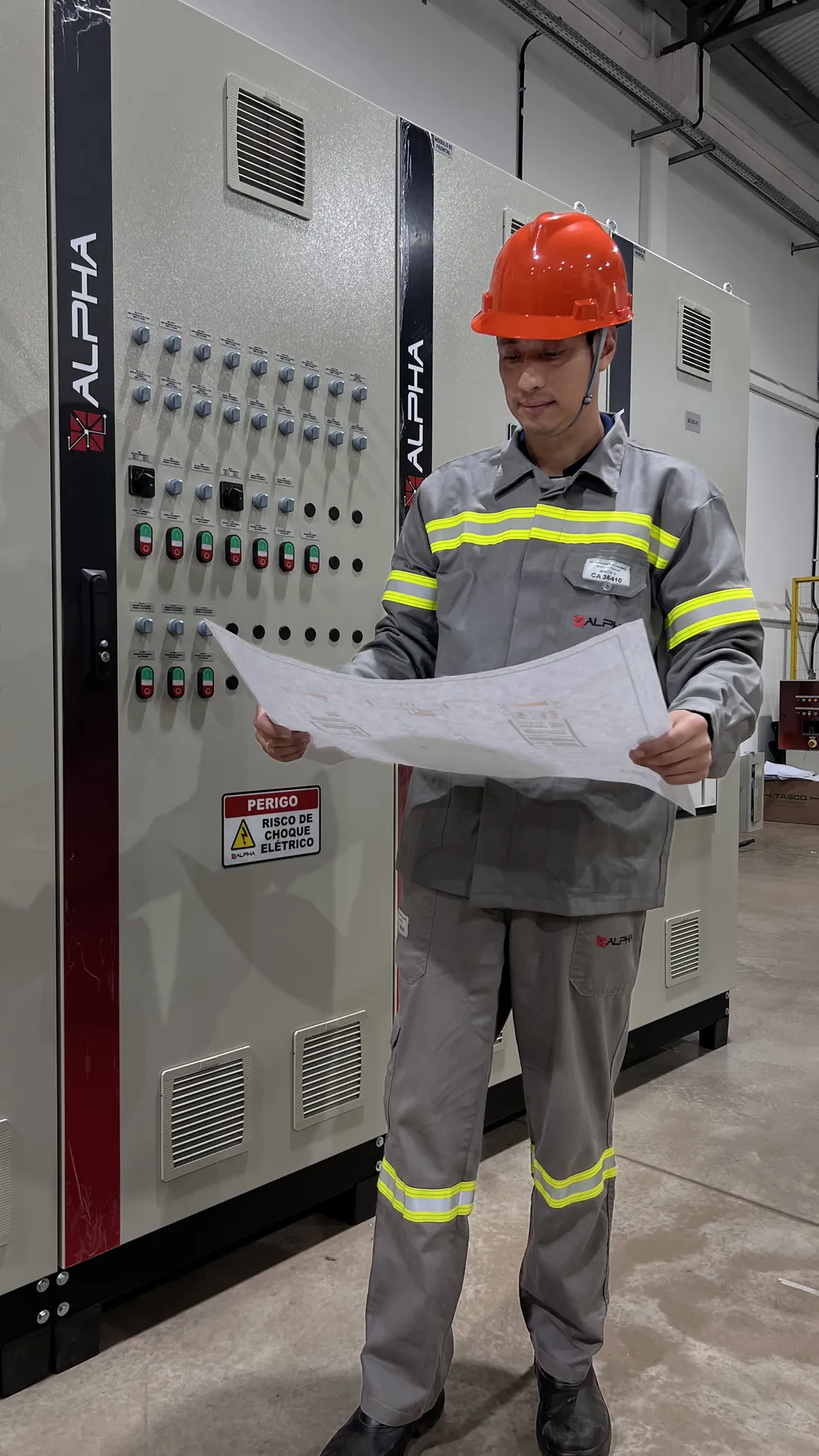 Profissional da Alpha conferindo o projeto diante de um painel elétrico de fábrica própria